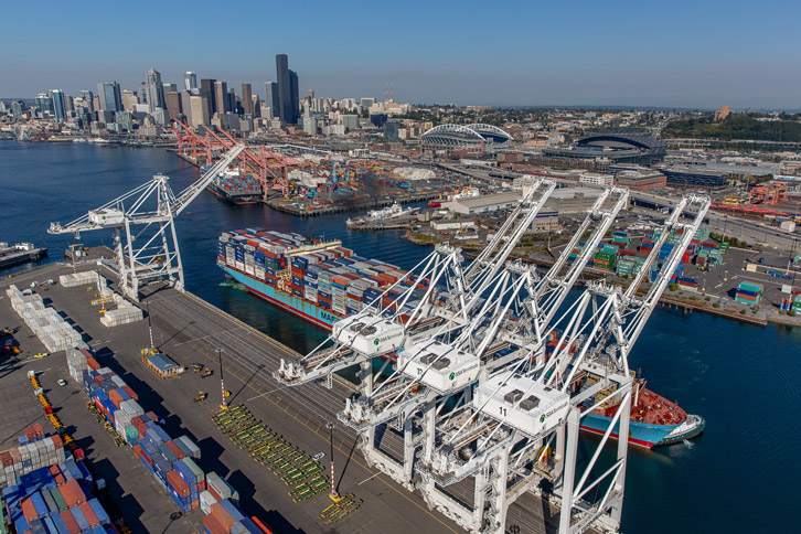 Terminal 5 is shown on the coast of Elliott Bay, with a backdrop of downtown Seattle. A barge is arriving, showing typical cargo operations. 